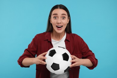 Surprised fan holding soccer ball on light blue background