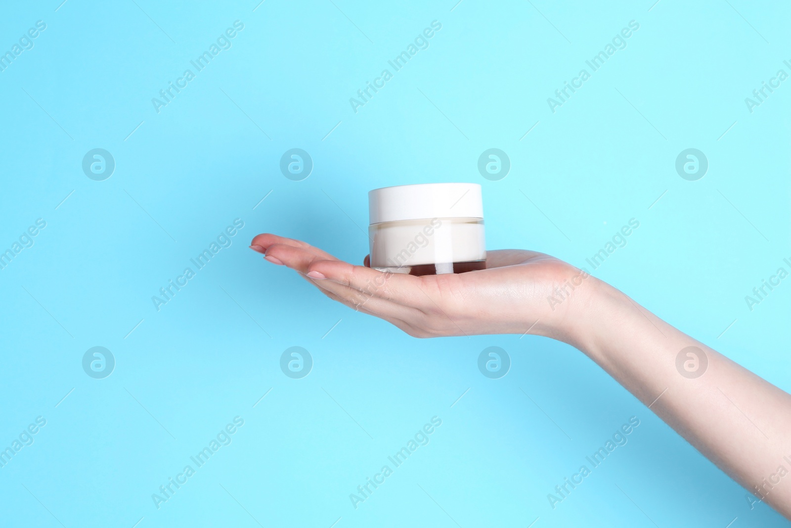 Photo of Woman holding jar of cream on light blue background, closeup. Space for text