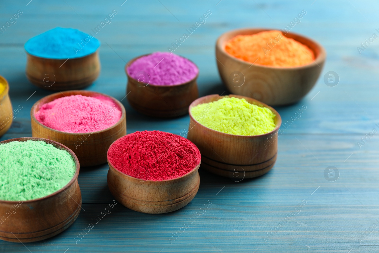 Photo of Colorful powder dyes on light blue wooden background, closeup. Holi festival