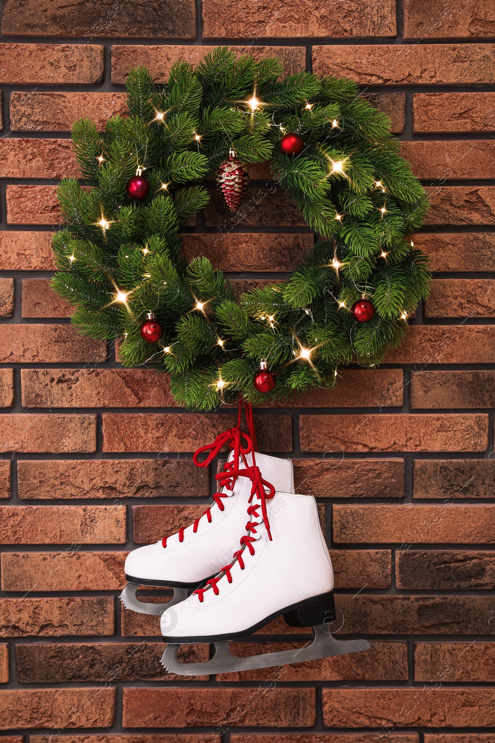 Photo of Pair of ice skates and beautiful Christmas wreath hanging on brick wall