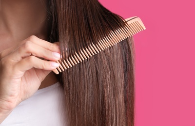 Photo of Young woman with wooden hair comb on color background, closeup. Space for text