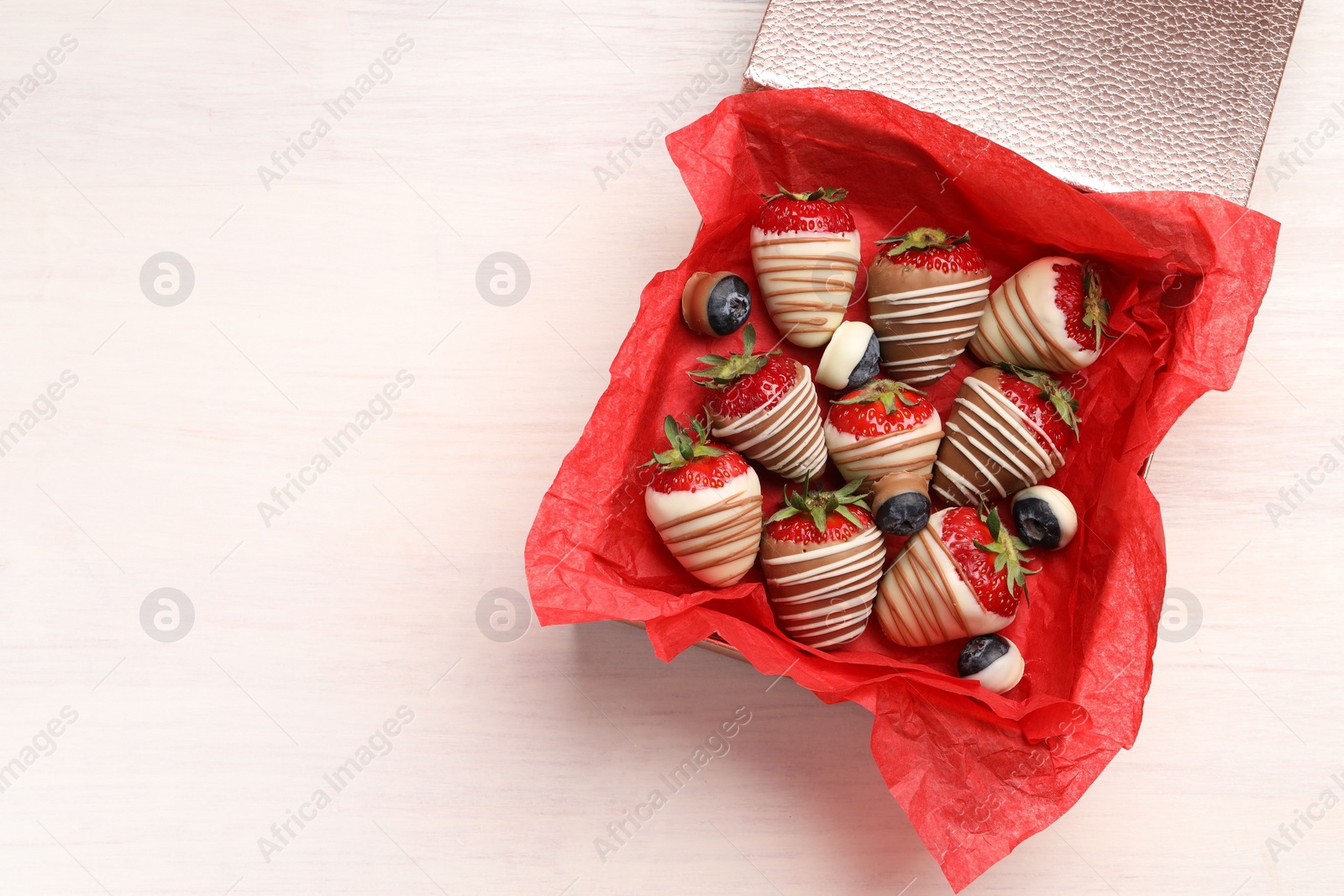 Photo of Box with delicious chocolate covered strawberries and blueberries on white table, top view. Space for text