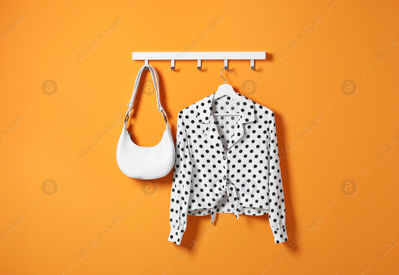 Photo of Hanger with polka dot shirt and bag on orange wall