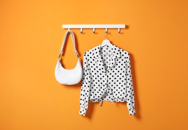 Photo of Hanger with polka dot shirt and bag on orange wall