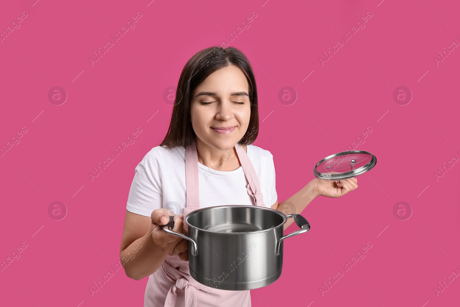 Photo of Happy young woman with cooking pot on pink background