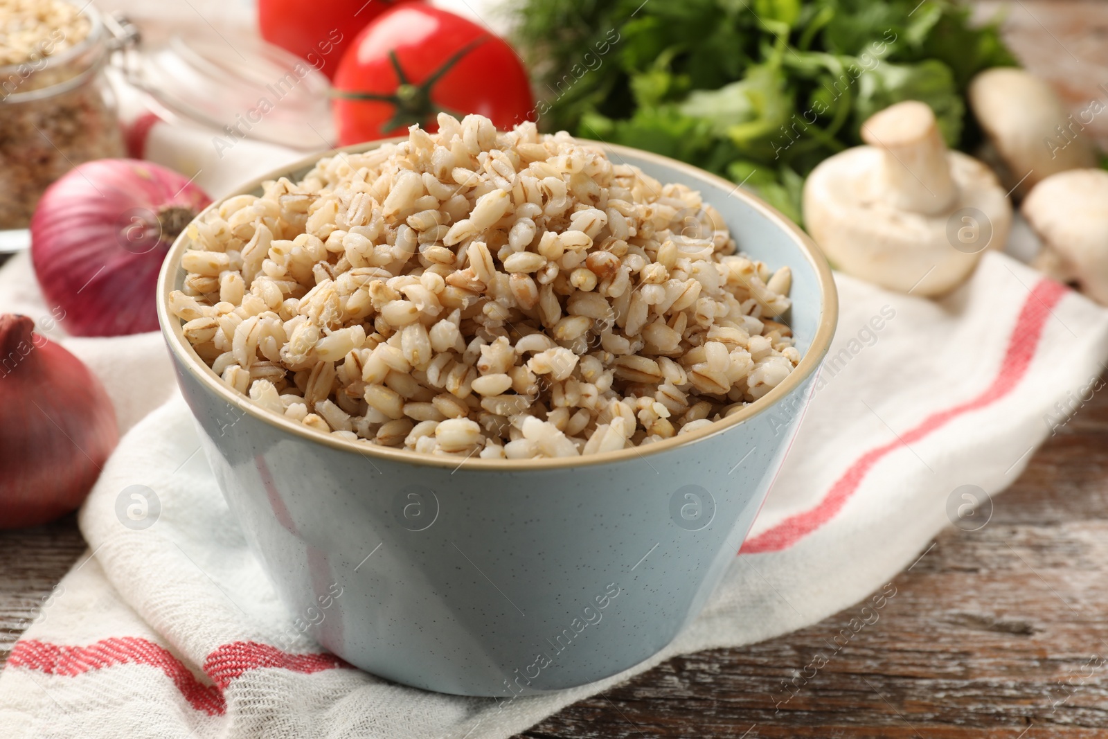 Photo of Delicious pearl barley in bowl served on wooden table, closeup