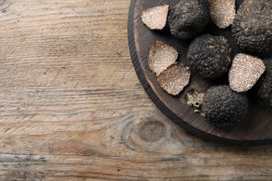 Photo of Whole and cut black truffles with board on wooden table, top view. Space for text