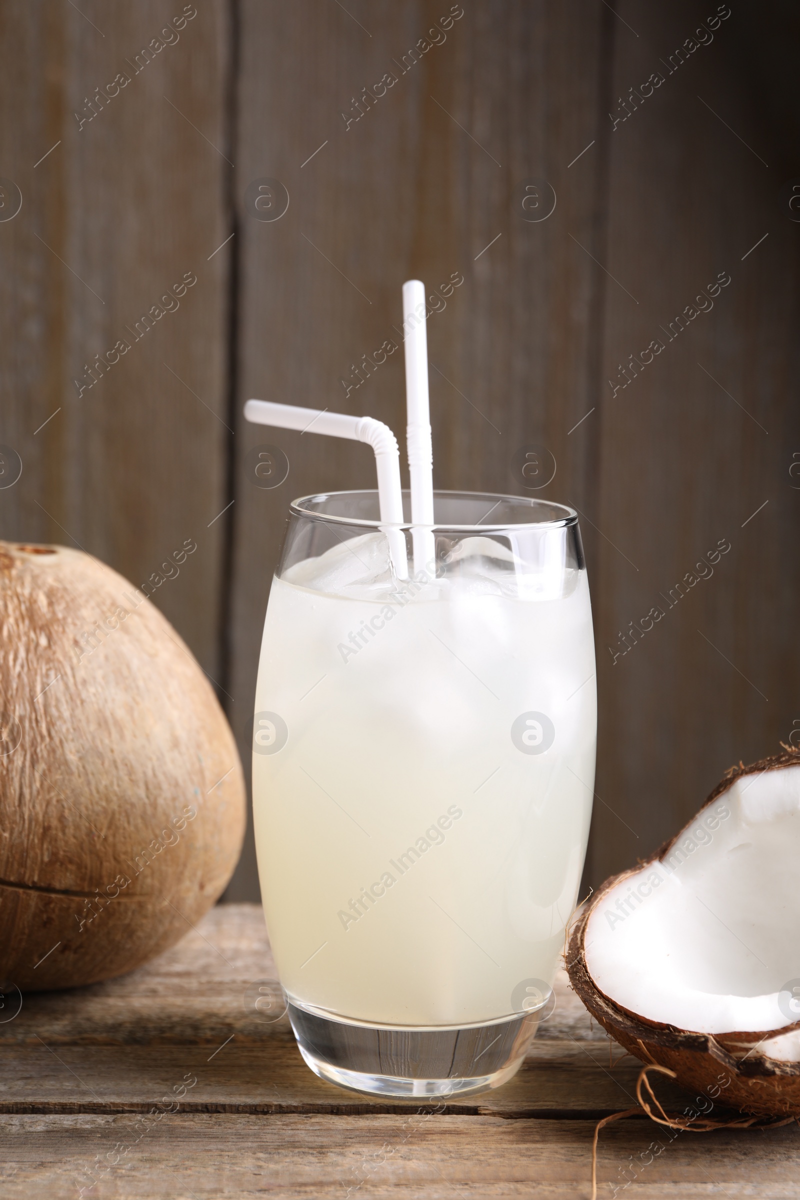 Photo of Glass of coconut water, ice cubes and nuts on wooden table