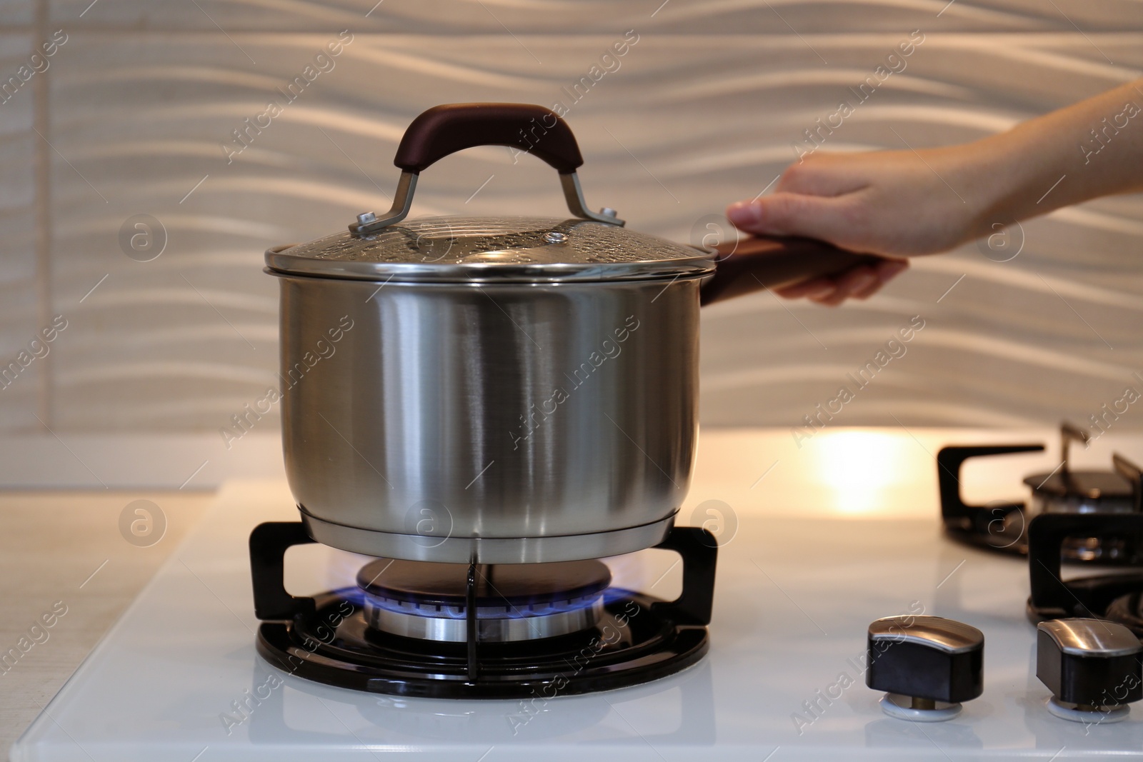 Photo of Woman cooking food in pot on modern kitchen stove with burning gas indoors, closeup