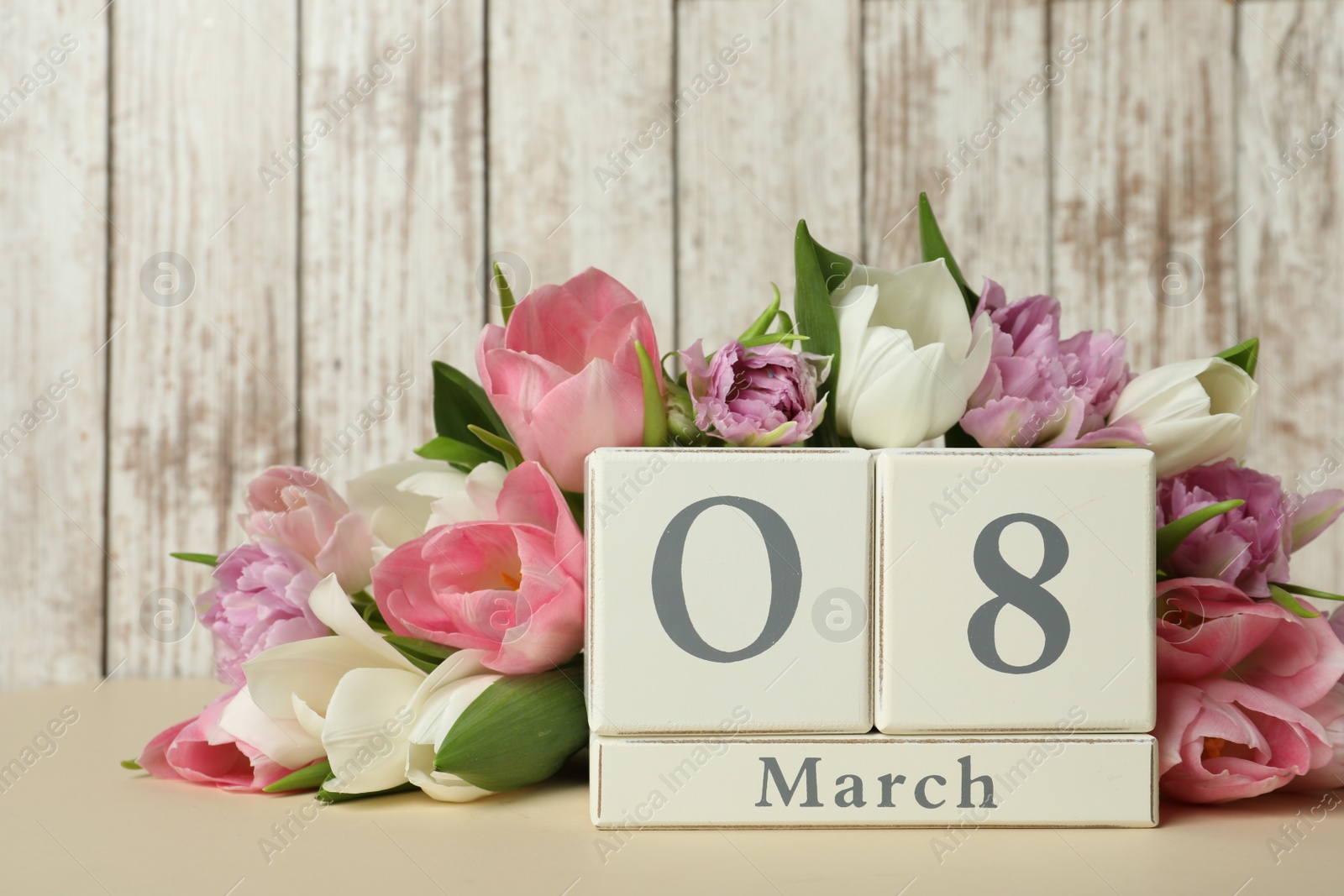 Photo of Block calendar with date 8th of March and tulips on table against wooden background. International Women's Day