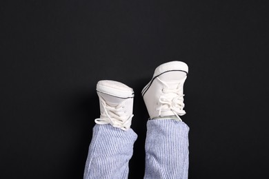 Photo of Little baby in stylish gumshoes on black background, top view
