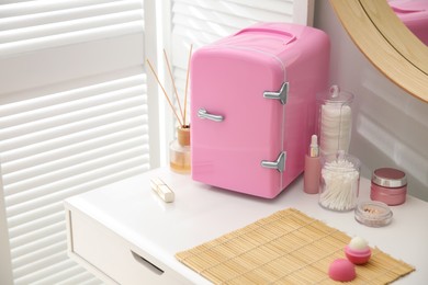 Photo of Cosmetics refrigerator and skin care products on white vanity table indoors