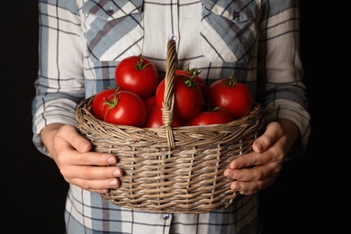 Woman with basket of ripe tomatoes on black background, closeup