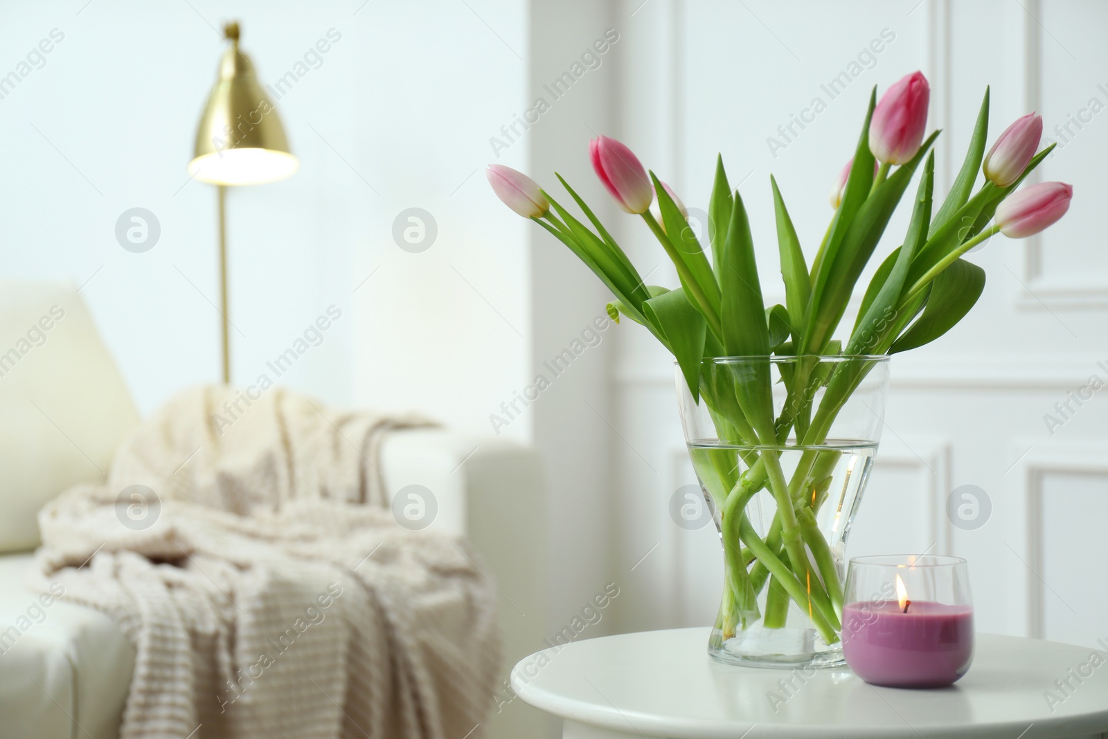 Photo of Beautiful tulips and burning candle on white table indoors, space for text. Interior design