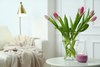 Beautiful tulips and burning candle on white table indoors, space for text. Interior design