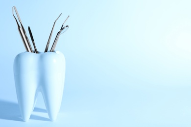 Photo of Tooth shaped holder with different dentist tools on color background. Space for text