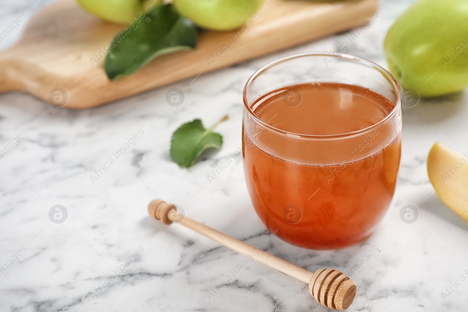 Photo of Glass of honey, apples and dipper on marble table