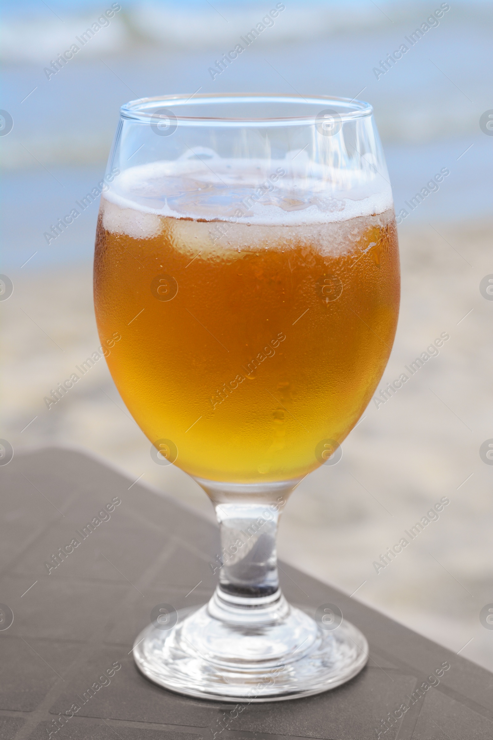 Photo of Cold beer in glass on beach, closeup