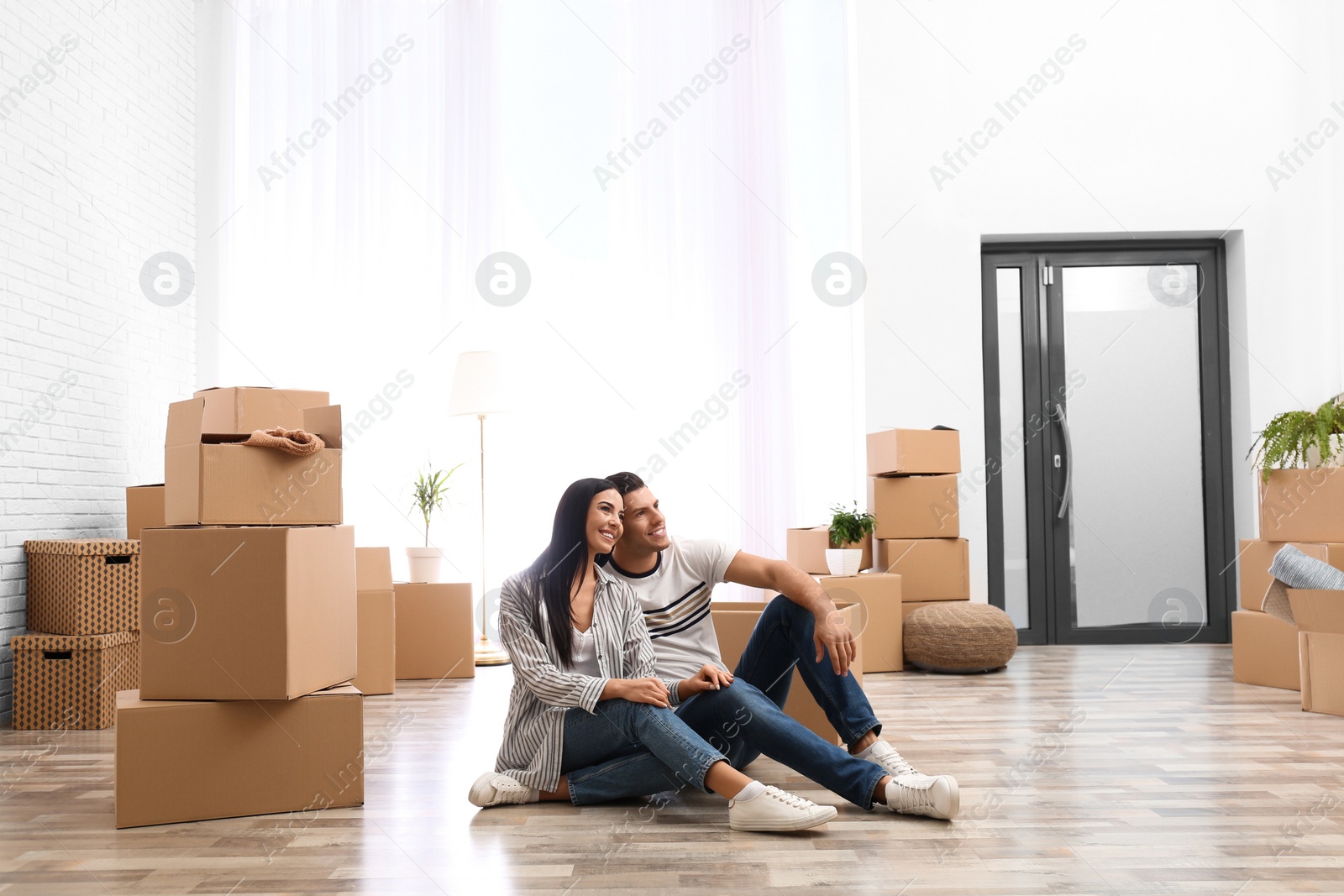 Photo of Happy couple in room with cardboard boxes on moving day