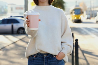 Photo of Woman holding pink takeaway cardboard cup on city street, closeup. Coffee to go