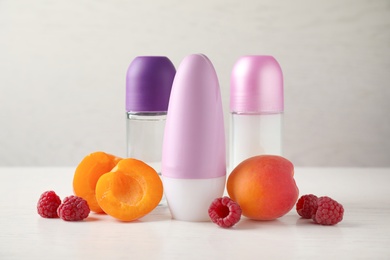Photo of Natural roll-on deodorants with apricots and raspberries on white wooden table