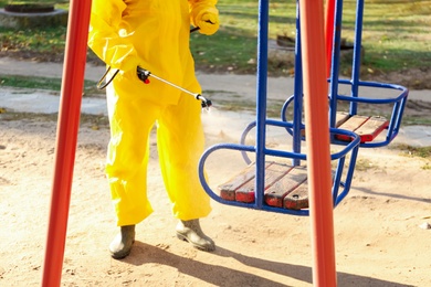 Photo of Person in hazmat suit with disinfectant sprayer cleaning children's playground, closeup. Surface treatment during coronavirus pandemic