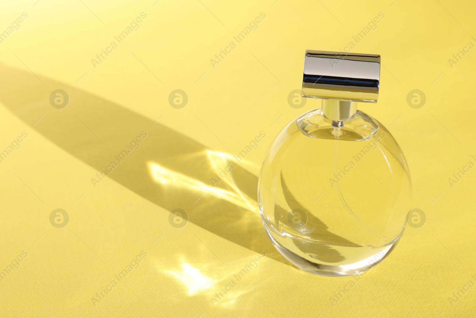 Photo of Luxury women's perfume. Sunlit glass bottle on yellow background. Space for text