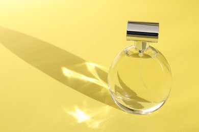 Luxury women's perfume. Sunlit glass bottle on yellow background. Space for text