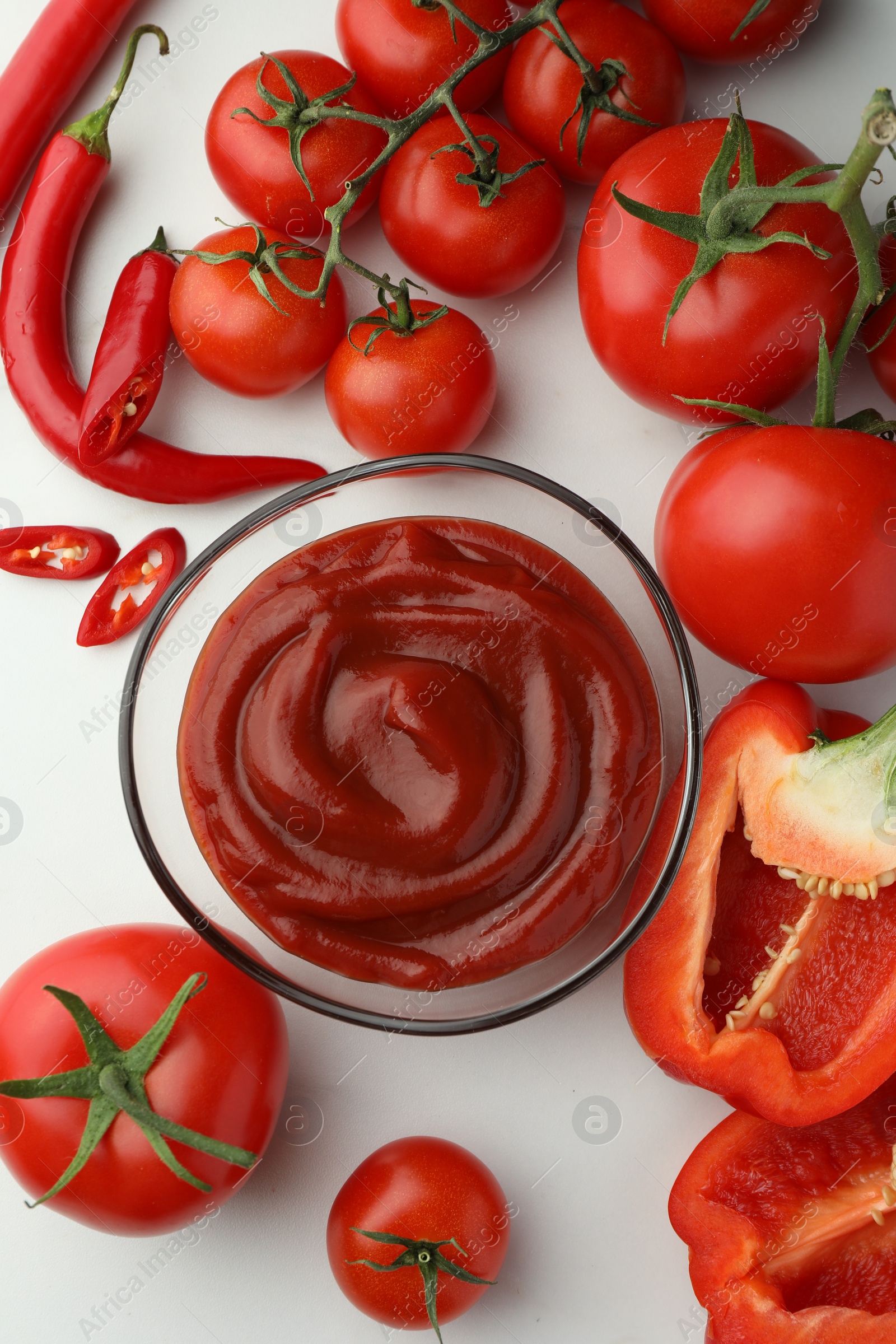 Photo of Bowl of tasty ketchup, tomatoes and peppers on white marble table, flat lay