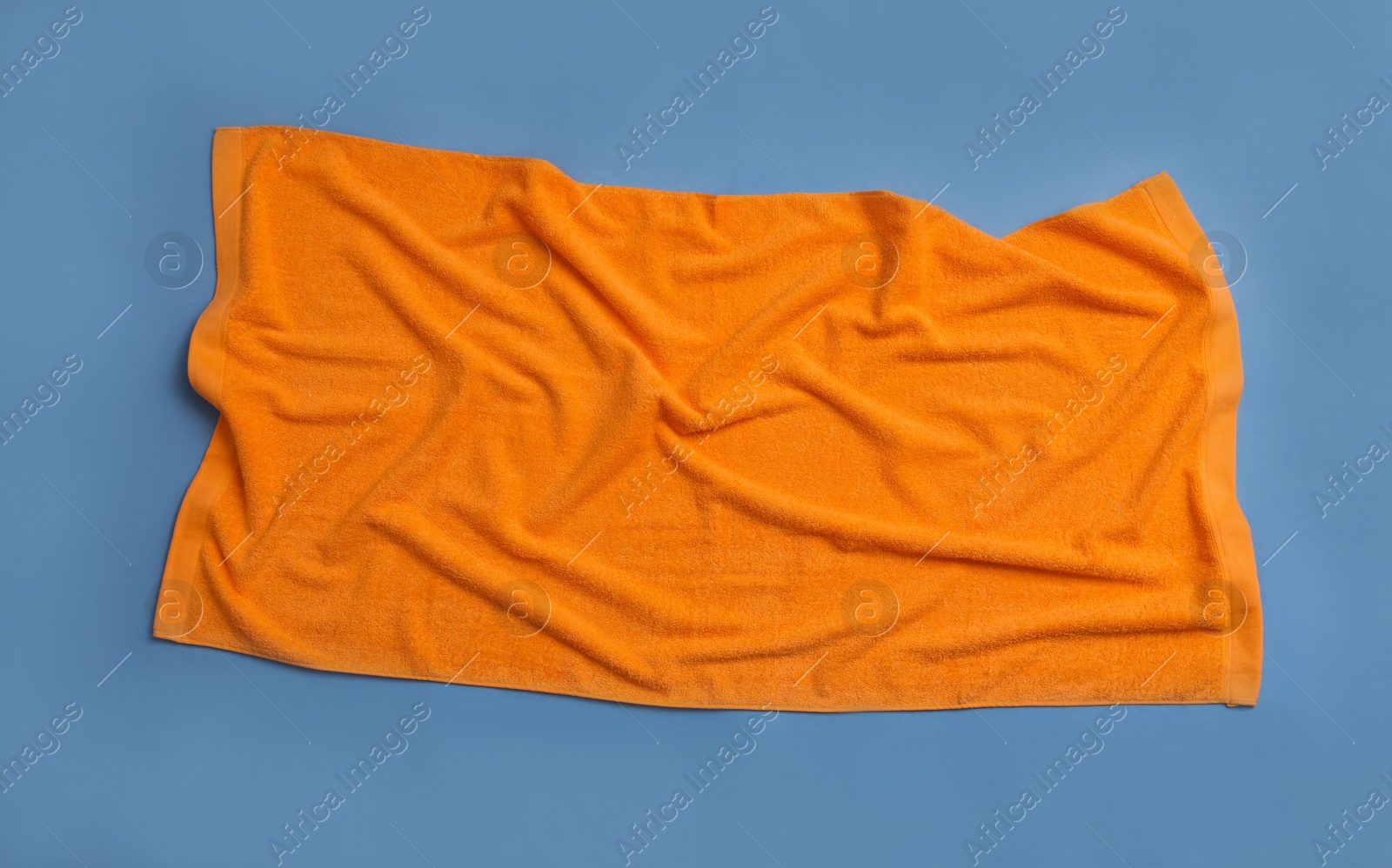 Photo of Crumpled orange beach towel on blue background, top view