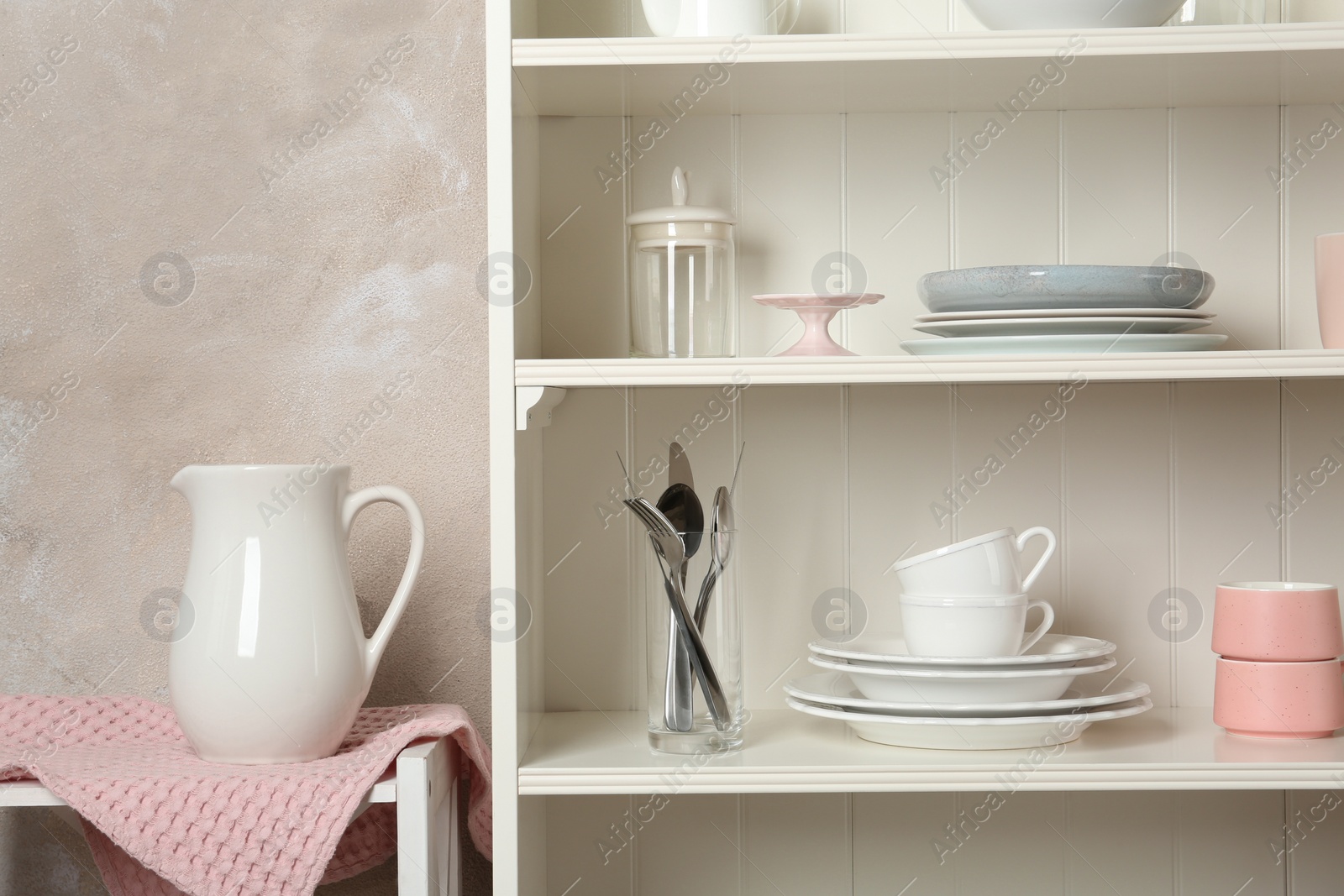 Photo of White shelving unit with set of dishware near wall