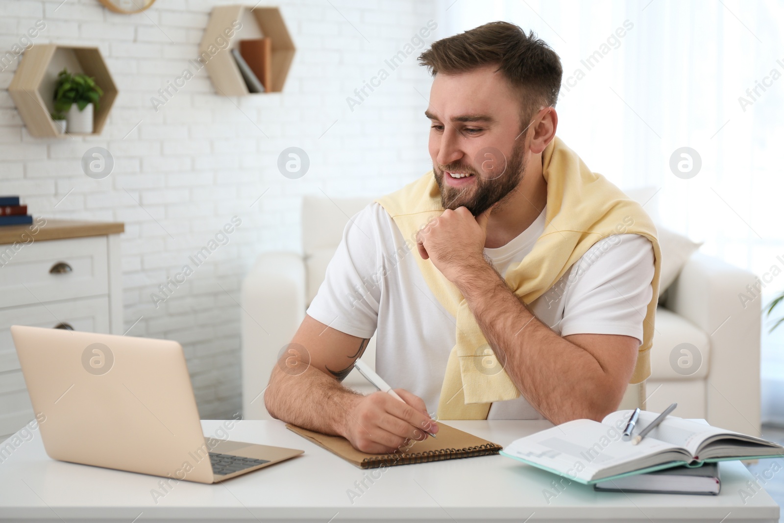 Photo of Young man taking notes during online webinar at table indoors