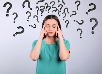 Image of Amnesia. Confused young woman and question marks on light background