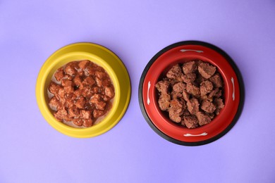 Wet pet food in feeding bowls on violet background, flat lay