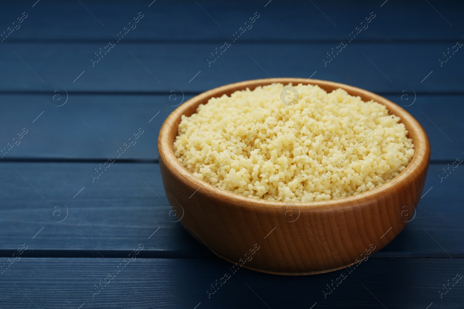 Photo of Bowl of tasty couscous on blue wooden table, closeup. Space for text