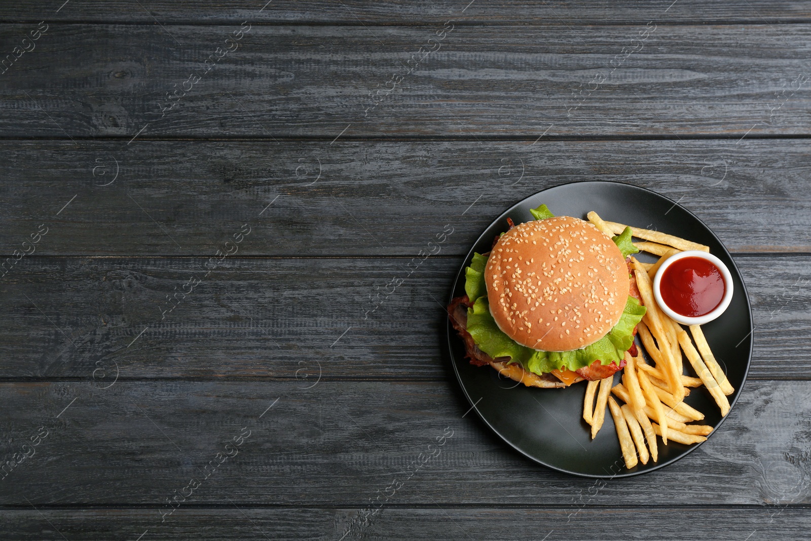 Photo of Plate with tasty burger, french fries and sauce on wooden background, top view. Space for text