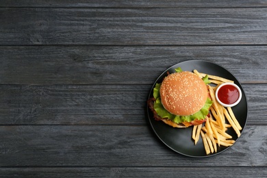 Photo of Plate with tasty burger, french fries and sauce on wooden background, top view. Space for text