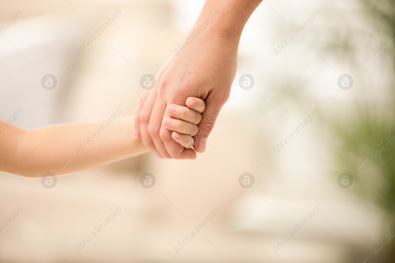 Photo of Mother holding hands with her child indoors, closeup. Happy family