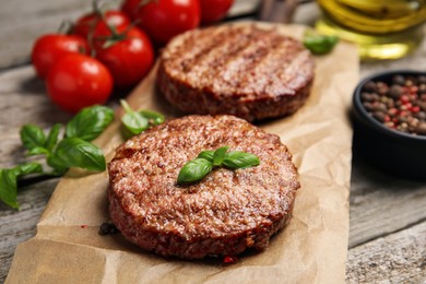 Tasty grilled hamburger patties with cherry tomatoes and seasonings on wooden table, closeup