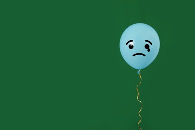 Image of Light blue balloon with sad face on green background. Space for text
