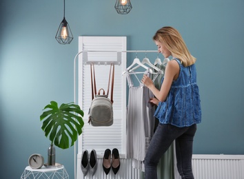 Photo of Young woman near clothes rack. Stylish dressing room interior