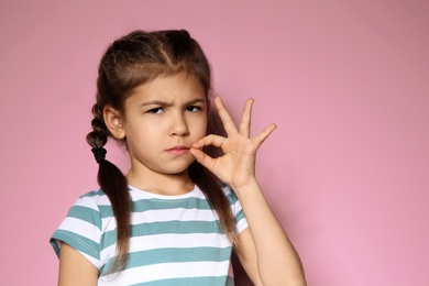 Photo of Little girl zipping her mouth on color background, space for text. Using sign language
