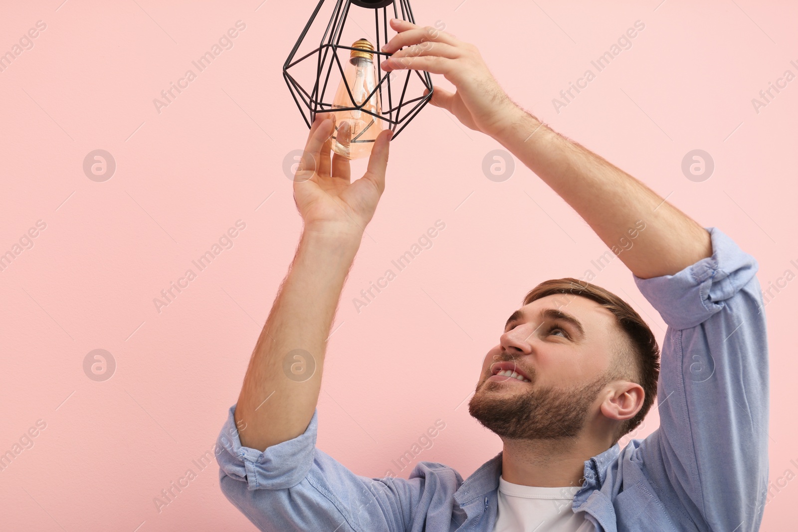 Photo of Man changing light bulb in lamp on color background