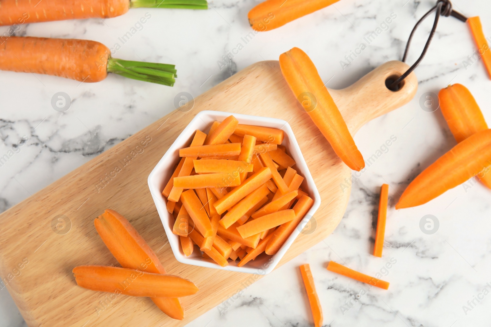 Photo of Bowl with cut ripe carrot on wooden board, top view