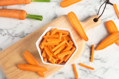 Bowl with cut ripe carrot on wooden board, top view