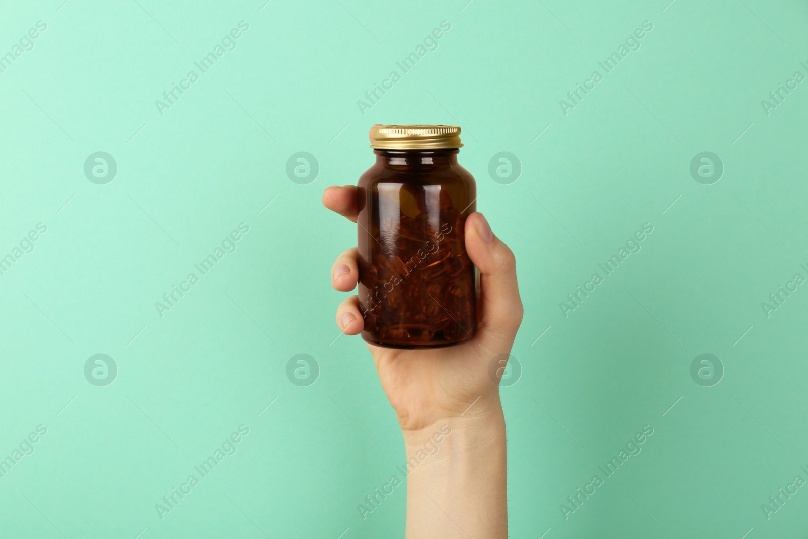 Photo of Woman holding jar with vitamin capsules on turquoise background, closeup