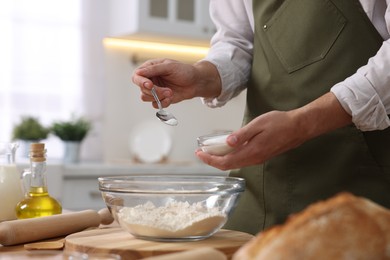 Photo of Making bread. Man putting salt into bowl with flour at wooden table in kitchen, closeup