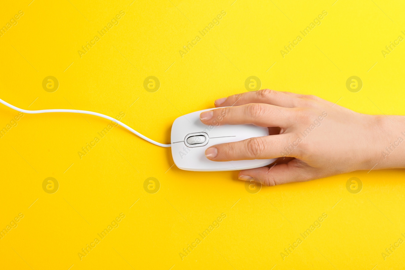 Photo of Woman using modern wired optical mouse on yellow background, top view