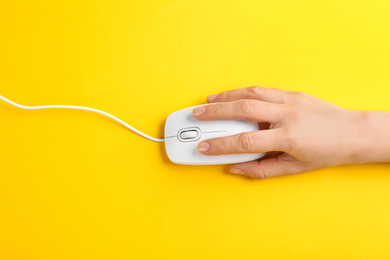 Photo of Woman using modern wired optical mouse on yellow background, top view