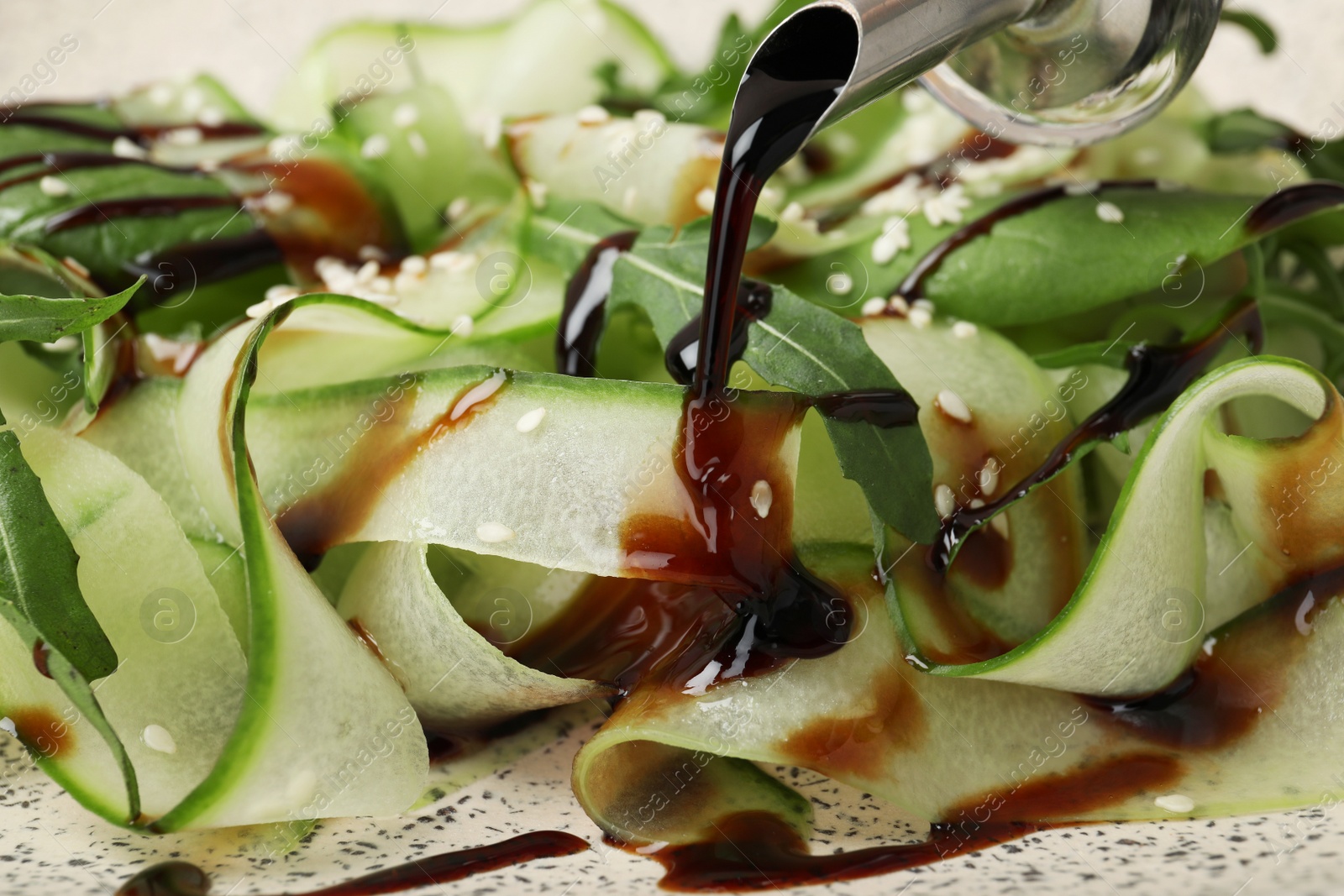 Photo of Pouring balsamic vinegar onto vegetable salad, closeup